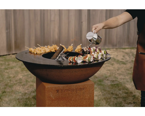 TigerFire Grill mit Spießen und Person, die Öl hinzufügt