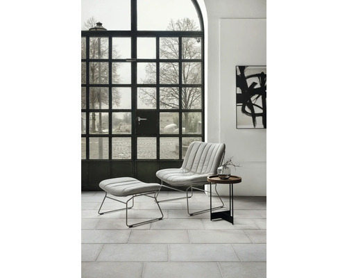 Salon moderne avec fauteuil, repose-pieds et table d''appoint devant une fenêtre à croisillons.