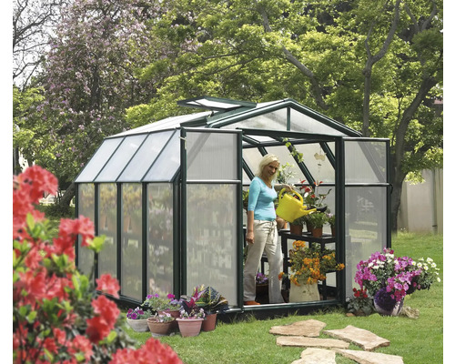 Serre avec des plantes et une femme arrosant avec un arrosoir dans le jardin.