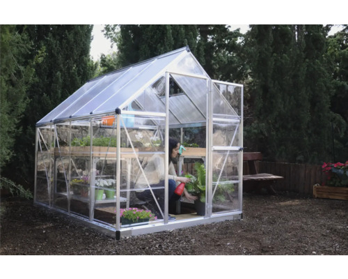 Gewächshaus mit Regalen und einer Person, die eine Pflanze giesst, im Garten