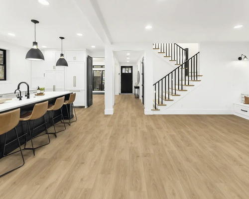 Pièce lumineuse avec cuisine ouverte, escalier et revêtement de sol en vinyle aspect bois.