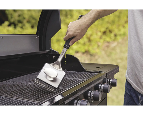 Eine Person reinigt den Grillrost mit einer Grillbürste.