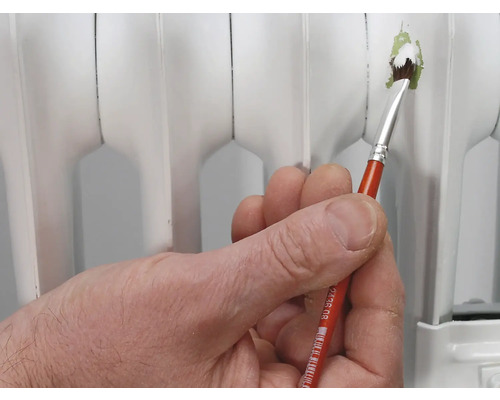Une main tient un pinceau pour peindre un radiateur.