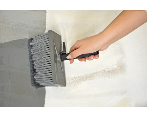 Une personne peint un mur avec une brosse de surface.