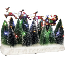 Village de Noël décoratif avec le Père Noël dans son traîneau tiré par des rennes, au milieu de sapins illuminés.