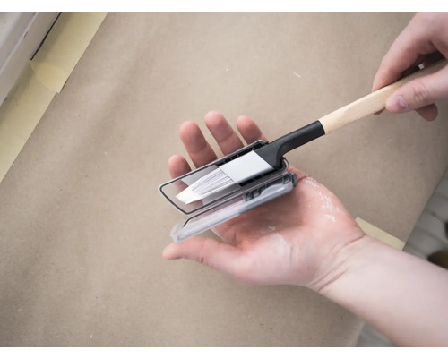 Un pinceau avec boîte de peinture est tenu par une main.