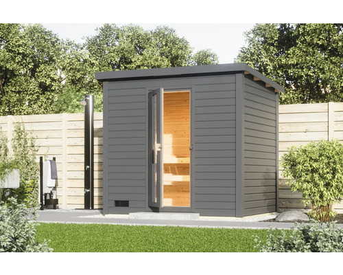 Chalet sauna Karibu Talos 3 avec poêle 9 KW et commande intégr. et porte en bois et verre isolant gris terre cuite Scène de jardin avec un sauna extérieur gris avec des portes en verre ouvertes et une douche extérieure.